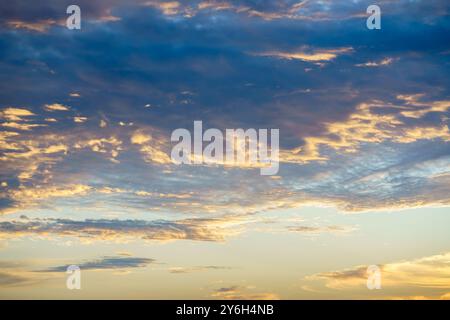 La lumière dorée du soleil traverse des couches de nuages sombres et clairs dans un vaste ciel. Banque D'Images