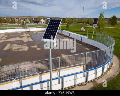 Airdrie Alberta Canada, 05 mai 2024 : panneaux solaires chargeant des lumières extérieures prise de vue aérienne surplombant une patinoire extérieure et un terrain de basketball à un par communautaire Banque D'Images