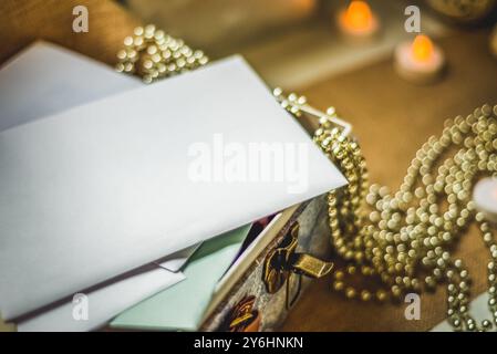 Photographie rapprochée d'enveloppes blanches et de lettres dans une boîte à charnières avec colliers de perles de couleur or et bougies chauffe-plat en arrière-plan Banque D'Images