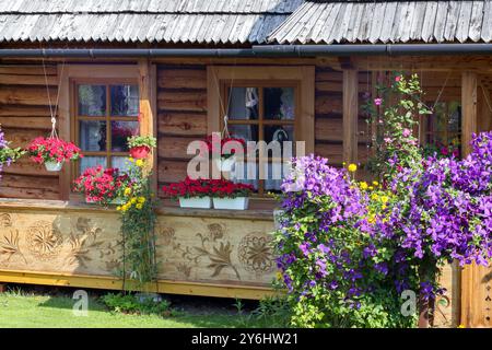 une vieille maison dans un village avec des sculptures en bois sur elle et un jardin fleuri Banque D'Images