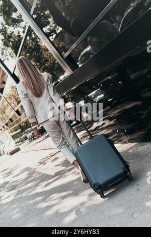 Femme d'affaires confiante. Vue arrière pleine longueur de la jeune femme en costume tirant des bagages tout en marchant à l'extérieur Banque D'Images