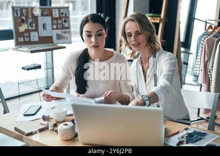 Transformer les idées en vêtements. Belles jeunes femmes travaillant sur des croquis et des échantillons tout en étant assis dans l'atelier Banque D'Images