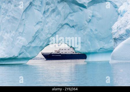 Île de Cuverville, péninsule Antarctique - 31 janvier 2024. Le navire d'expédition Antarctique L'aventurier océanique est ancré près de l'île de Cuverville sur la péninsule Antarctique et encadré par un iceberg au premier plan. Banque D'Images