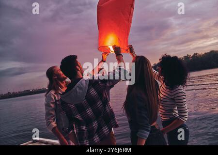 Amuse-toi bien. Groupe de jeunes en tenue décontractée tenant la lanterne du ciel tout en se tenant debout sur la jetée Banque D'Images