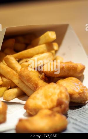 Sur la table, il y a une boîte de nuggets de poulet et de frites. Le repas comprend de la restauration rapide et de la nourriture frite, qui sont des plats de base populaires dans beaucoup Banque D'Images