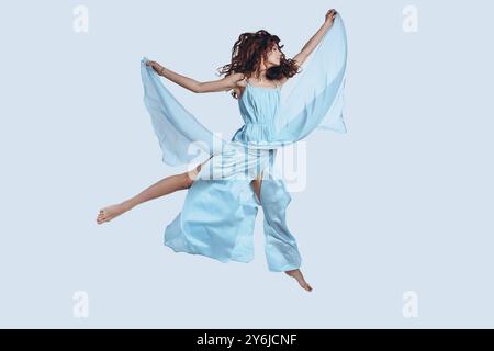 Se sentir libre de faire quoi que ce soit. Plein plan studio d'une jeune femme attrayante dans une robe élégante gardant les bras tendus tout en planant contre le gris Banque D'Images
