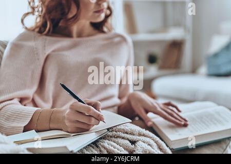 Se concentrer sur l'éducation. Gros plan de jeunes femmes écrivant quelque chose tout en étant assis sur le canapé à la maison Banque D'Images