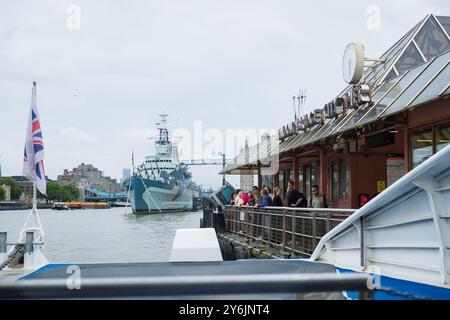 Londres, Royaume-Uni - 25 juillet 2024 : arrêt du bateau Uber à London Bridge City Pier sur la Tamise. Drapeau de la Grande-Bretagne agitant. Drapeau du Royaume-Uni dans le vent. Banque D'Images