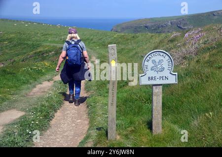 Femme marchant près du panneau National Trust pour Bre-Pen et panneau en bois pour Mawgan Porth on the Path on the Southwest Coastal Path, North Cornwall, Royaume-Uni. Banque D'Images