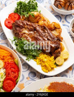 Épaule d'agneau braisée iranienne servie avec des herbes fraîches, des tomates grillées et des accompagnements traditionnels. Banque D'Images