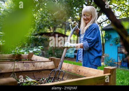 Femme âgée pelletant du compost avec une fourche dans le jardin Banque D'Images