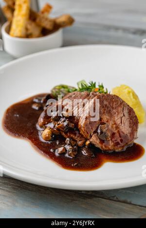 Filet de bœuf grillé avec sauce demi-glace et légumes grillés sur une assiette en porcelaine blanche Banque D'Images