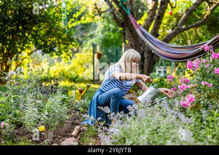 Femme mature arrosant les plantes dans son jardin un jour d'été ensoleillé Banque D'Images