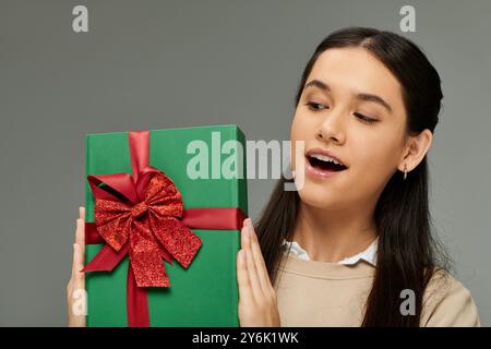 La femme affiche le plaisir comme elle tient un cadeau magnifiquement enveloppé orné d'un arc. Banque D'Images