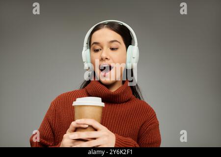 Une jeune femme avec des écouteurs sourit largement, savourant son café dans une atmosphère détendue. Banque D'Images