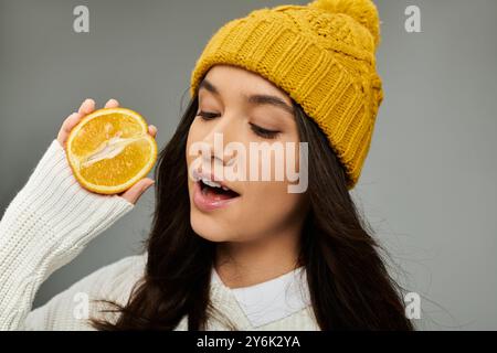 Une jeune femme avec un chapeau vibrant tient joyeusement une tranche d'agrumes, rayonnant de bonheur. Banque D'Images