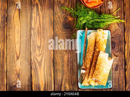 Crêpes minces ou crêpes avec saumon fumé, et aneth sur un fond de bois foncé. Mise au point sélective Banque D'Images