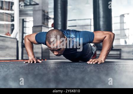 En poussant fort. Beau jeune homme africain dans des vêtements de sport faisant des push-ups tout en faisant de l'exercice dans la salle de gym Banque D'Images