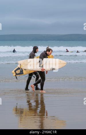 Deux amis surfeurs portant leurs planches de surf marchant le long du rivage sur la plage de Towan à Newquay en Cornouailles au Royaume-Uni. Banque D'Images