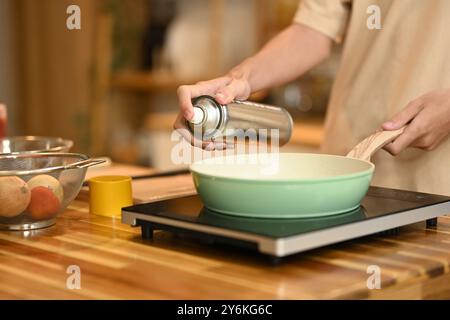 Fermez la femme pulvérisant de l'huile de cuisson sur la poêle à frire sur la cuisinière Banque D'Images