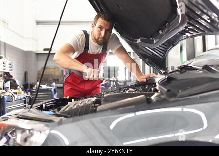 mécanicien automobile en vêtements de travail travaille dans un atelier et répare un véhicule Banque D'Images