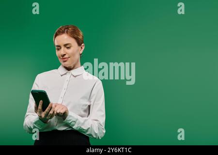 Une femme professionnelle vêtue d’une chemise blanche interagit avec son smartphone dans un environnement animé. Banque D'Images