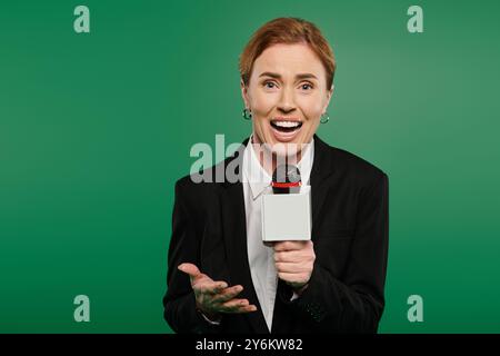 Un présentateur de télévision vibrant dans une élégante tenue noire interagit avec enthousiasme, microphone à la main. Banque D'Images