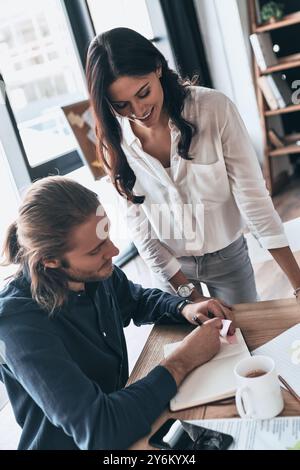 En passant en revue les détails. Vue de dessus de jeunes collègues modernes en vêtements décontractés élégants travaillant ensemble et souriant tout en passant du temps dans le bureau créatif Banque D'Images