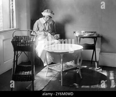 Ordre du bain. Infirmière assise sur une chaise basse, portant mackintosh et tabliers en flanelle, avec bébé sur ses genoux. Le bain est en face d'elle, panier d'un côté et table contenant lotion boracique, coton, etc, de l'autre. Les vêtements de bébé, disposés dans le bon ordre à mettre, et les serviettes turques et faciales devraient être aérées sur le garde-feu à ses côtés. Banque D'Images