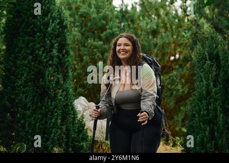 Une femme joyeuse de grande taille marche à travers une forêt luxuriante, embrassant la beauté et l'aventure de la nature. Banque D'Images