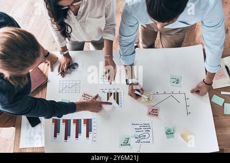 En passant en revue les détails. Gros plan vue de dessus de jeunes gens d'affaires confiants travaillant ensemble tandis que l'homme écrivant sur le plan dans le bureau Banque D'Images