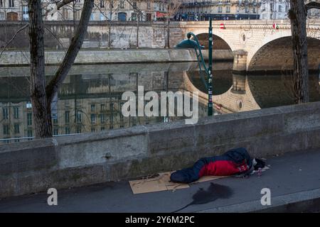 France, Paris, 75, 4ème arrondissement, Quai des Celestins, personne sans-abri allongée dans une couette sur une boîte en carton au sol, février 2023. Banque D'Images