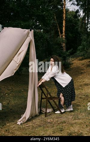 Une femme de taille plus confiante s'appuie contre une chaise en bois, profitant de la tranquillité de la nature. Banque D'Images