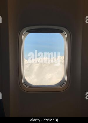 Nuages moelleux avec une lueur chaude vus à travers une fenêtre d'avion.' Banque D'Images