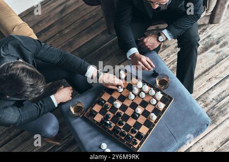 Réfléchissez bien avant le déménagement. Vue de dessus de jeunes hommes réfléchis en costumes complets jouant aux échecs tout en étant assis à l'intérieur Banque D'Images