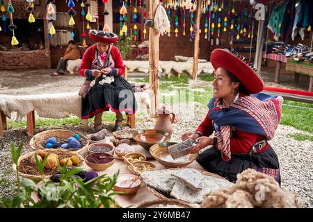 Deux femmes en tenue traditionnelle péruvienne fabriquent des textiles dans un marché animé de Chinchero. Des fils colorés et des tissus locaux mettent en valeur la riche culture péruvienne Banque D'Images