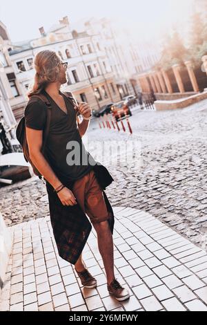 Nouvelle aventure. Pleine longueur de jeune homme dans des vêtements décontractés regardant le coucher du soleil tout en marchant à l'extérieur Banque D'Images