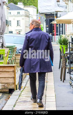 Vue arrière d'un homme portant un imperméable et portant un parapluie marchant sur le trottoir - Tours, Indre-et-Loire (37), France. Banque D'Images