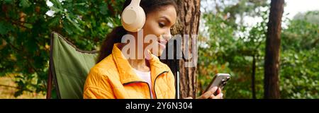 Une jeune femme afro-américaine se détend dans la forêt, profitant des couleurs d'automne et de la musique sur son téléphone. Banque D'Images