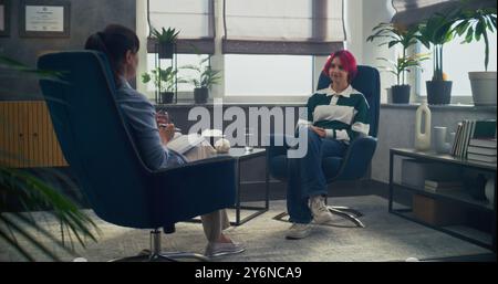 Dans la salle de psychothérapie, l'adolescente parle à son thérapeute, partage des émotions positives pendant la séance de conseil. Vue arrière de la psychologue féminine assise dans la chaise, fournissant la thérapie pour l'adolescent. Banque D'Images