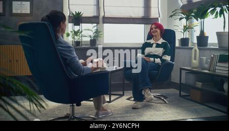 Dans la salle de psychothérapie, l'adolescente parle à son thérapeute, partage des émotions positives pendant la séance de conseil. Vue arrière de la psychologue féminine assise dans la chaise, fournissant la thérapie pour l'adolescent. Banque D'Images