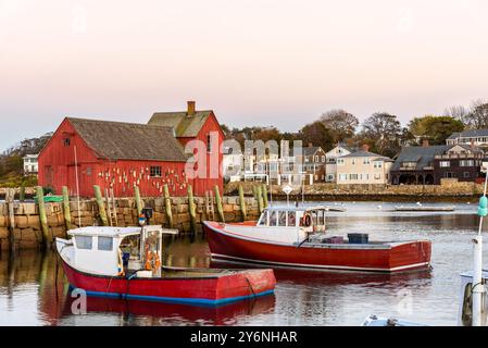 Cabane de pêche boisée rouge sur un quai de pierre dans un port de pêche entouré de bâtiments résidentiels au crépuscule en automne Banque D'Images