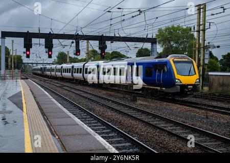 Train électrique moderne qui accélère le long des voies sous un ciel orageux, mettant en valeur le transport quotidien. Banque D'Images