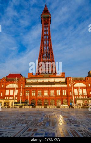 La tour emblématique de Blackpool baignée par la lumière du coucher du soleil, avec la façade du bâtiment historique et la promenade à motifs. Banque D'Images