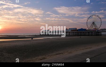 Coucher de soleil tranquille sur un quai de plage avec une grande roue, projetant une lueur chaude sur le paysage serein. Banque D'Images