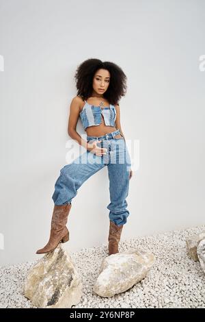 Une belle jeune femme afro-américaine met en valeur son sens de la mode dans une tenue en denim à la mode. Banque D'Images