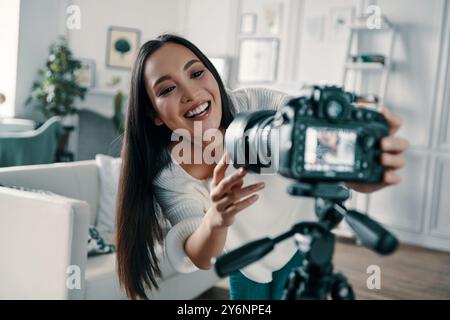 Vérification de l'équipement multimédia. Jeune femme attirante ajustant la caméra vidéo et souriant tout en faisant une nouvelle vidéo pour son blog Banque D'Images