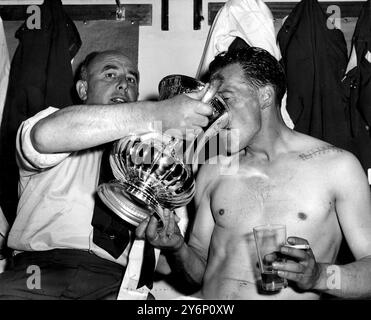 3 mai 1958 : vainqueurs de la finale de la FA Cup. Bolton Wanderers (2) contre Manchester United (0). Photo montre : le capitaine et attaquant central de Bolton Wanderers, Nat Lofthouse, qui a marqué les deux buts de son équipe, reçoit un verre de leur manager, Bill Ridding dans le vestiaire de Wembley. Une rangée de points de suture peut être vue sur l'épaule de Lofthouse, où une épingle a été insérée après sa blessure récente. Banque D'Images