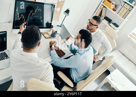 En passant en revue les détails. Vue de dessus de jeunes hommes modernes en vêtements de forme travaillant à l'aide d'ordinateurs tout en étant assis dans le bureau Banque D'Images