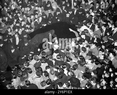 Un policier allongé sur le toit de la voiture et d'autres sur le capot tentent de tenir à la baie A. pressant foule de milliers de fans frénétiques et et et forcer un passage pour le roi américain Rock'n'Roll Bill Haley sur son arrivée à Waterloo Station Londres ce soir le chef d'orchestre - ici pour une tournée de la Grande-Bretagne avec son groupe le Comets - avait voyagé de Southampton dans un train spécial rempli de 400 fans après avoir débarqué de la Cunard le paquebot Queen Elizabeth qui l'avait amené de New York le 5 février 1957 Banque D'Images